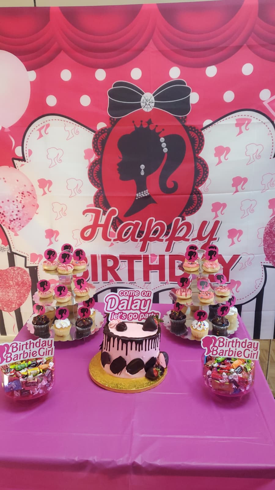 Full Barbie-inspired party table with pink balloon arch, desserts, and themed decorations