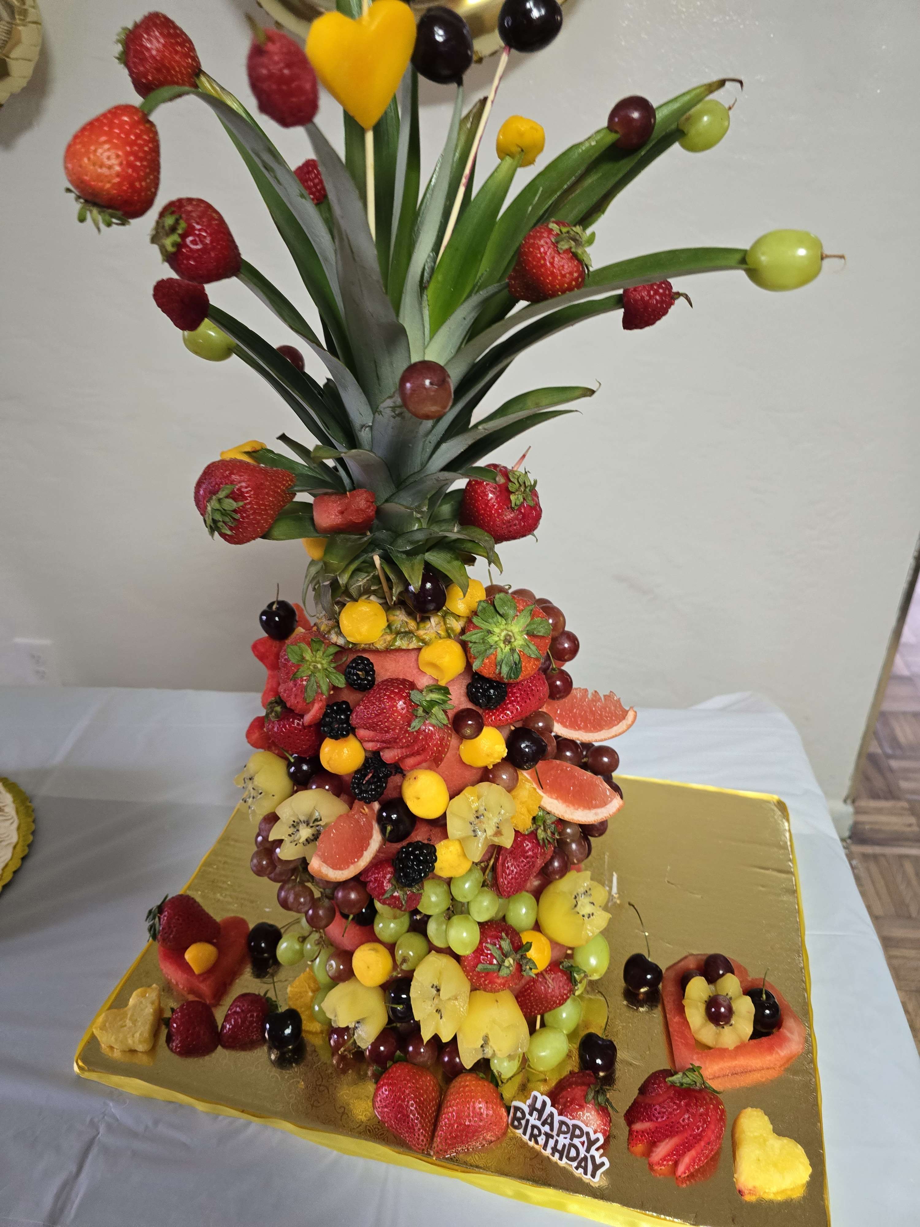 Tall custom fruit tower decorated with fresh berries, grapes, pineapple, and melon